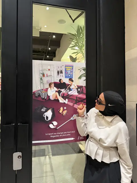 Amani montre l’affiche de la campagne collée sur une vitrine