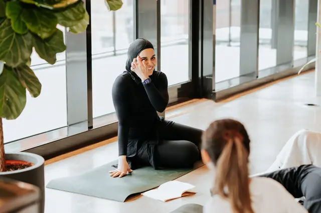 Amani montre un mouvement de pilates assise sur son tapis