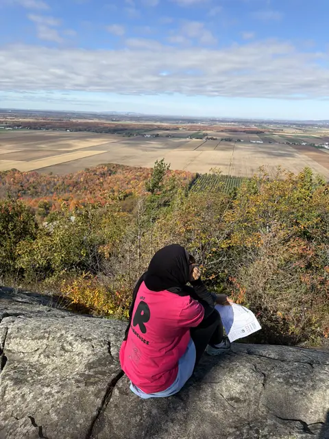Une Runneuse en t-shirt rose assise sur une falaise au-dessus d’une vallée d’automne